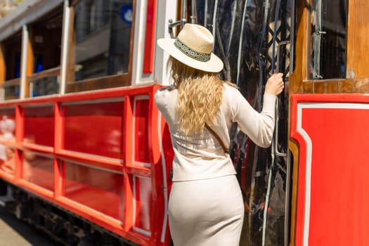 Beautiful young girl tourist in a hat poses in front of tram at popular Istiklal street in Beyoglu, Istanbul, Turkey .