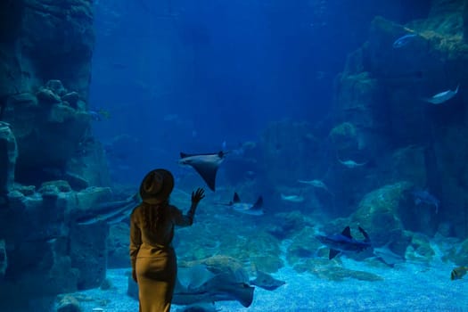 A young woman touches a stingray fish in an oceanarium tunnel.