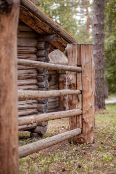 Large wooden fence posts that enclose an old wooden house in the forest. How people built houses and fences in the past. Ecological construction and materials.