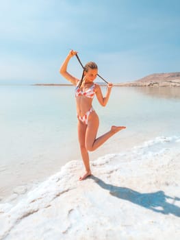 Beautigul girl in swimming suit on Dead sea salt crystals formation coastline, clear cyan green water at Ein Bokek beach, Israel. Dead sea resort holiday