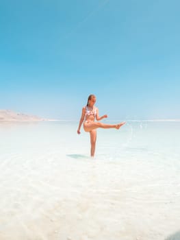 Beautigul girl in swimming suit on Dead sea salt crystals formation coastline, clear cyan green water at Ein Bokek beach, Israel. Dead sea resort holiday