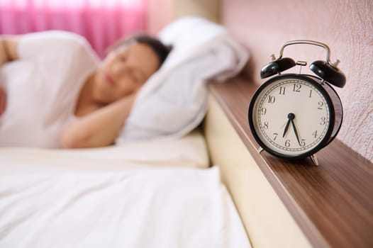 Selective focus on black alarm clock on blur background of pregnant woman, expectant mother sleeping, napping at daytime, renewing her energy, taking care of the health of her future baby. Pregnancy