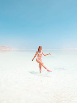 Beautigul girl in swimming suit on Dead sea salt crystals formation coastline, clear cyan green water at Ein Bokek beach, Israel. Dead sea resort holiday