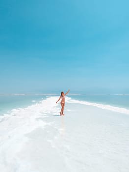 Beautigul girl in swimming suit on Dead sea salt crystals formation coastline, clear cyan green water at Ein Bokek beach, Israel. Dead sea resort holiday