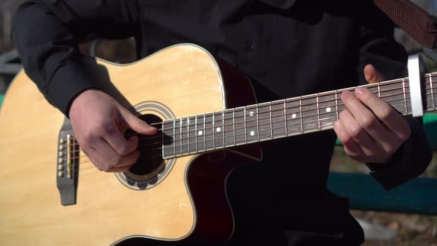 A young man plays the acoustic guitar while sitting in the park. A man plays the guitar close-up. The camera is moving. 4k