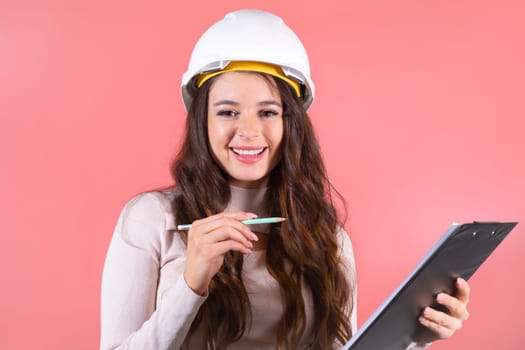 A happy brunette architect in a helmet checks the list on the pink background.