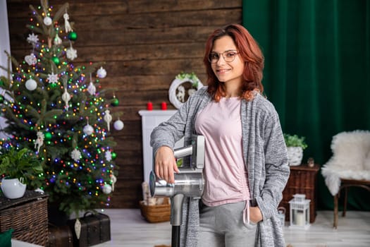 An attractive young girl holds a vacuum cleaner in her hand and smiles beautifully. It's time for a thorough cleaning of the whole house.