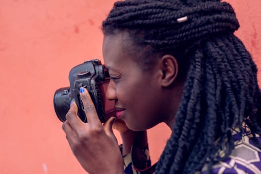 Close up portrait of beautiful young woman with braid hairstyle concentrated while making a photograph with reflex camera over a wall outdoors