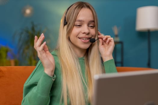 Caucasian woman wearing headset, freelance worker, call center or support service operator helpline, having talk with client or colleague communication support waving hello. Girl at home room on sofa
