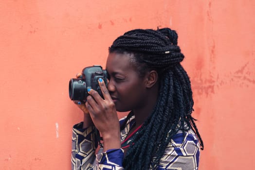 Close up portrait of beautiful young woman with braid hairstyle concentrated while making a photograph with reflex camera over a wall outdoors