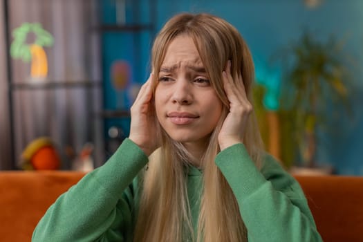 Displeased woman rubbing temples to cure headache problem, suffering from tension and migraine stress grimacing in pain high blood pressure at home room apartment. Teen child girl on couch. Lifestyles