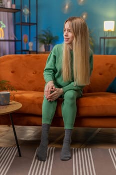 Young woman suffer from painful severe knee joint ache, leg muscles, could not walk. Portrait of Caucasian girl massaging her knees illness cramps rheumatism at home room on sofa. Health care problem