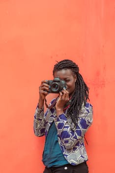 Close up portrait of beautiful young woman with braid hairstyle concentrated while making a photograph with reflex camera over a wall outdoors