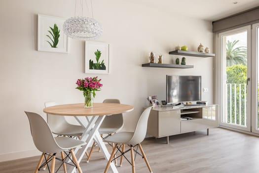 Cozy stylish living room with a round dining table, TV and panoramic windows and decorative accessories. The concept of a modern urban apartment for newlyweds.