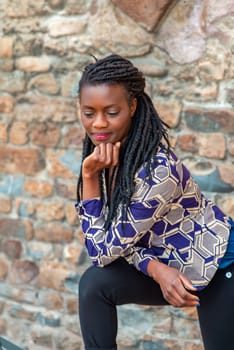 relaxed young black woman sitting. Stylish model. Braid dreadlock hairstyle. Confident African female in selective focus outdoors, fashion style, happiness concept. Outdoors.