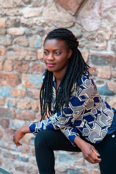 relaxed young black woman sitting. Stylish model. Braid dreadlock hairstyle. Confident African female in selective focus outdoors, fashion style, happiness concept. Outdoors.