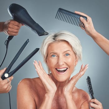 Hair care, excited and senior woman with hairdresser for beauty, haircut and preparation on grey studio background. Happy, smile and surprise face of an elderly model with hands of stylist for hair.