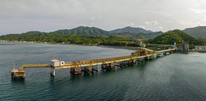 Long loading pier with rusted and equipment stretches into sea on coast. High quality photo