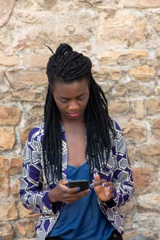 Close up portrait of beautiful young african american woman reading answering text message on mobile phone app over a wall outdoors