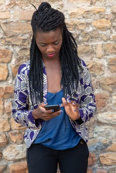 Close up portrait of beautiful young african american woman reading answering text message on mobile phone app over a wall outdoors
