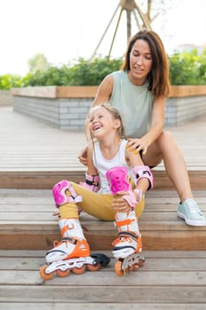 Little girl in roller skates and her mom sit on a wooden ladder and hug outdoors