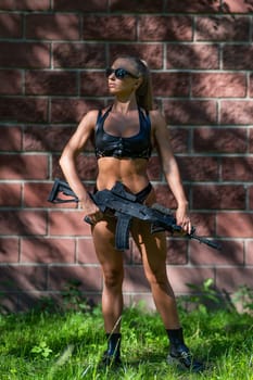 A caucasian woman in a bikini holds a machine gun against a brick wall