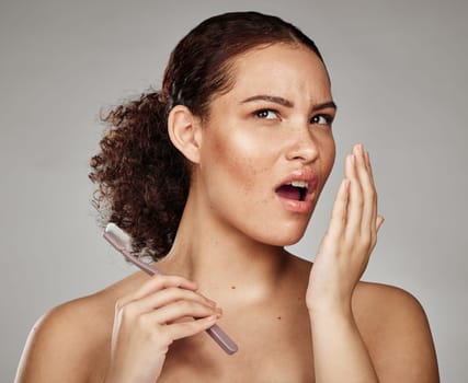 Woman, bad breath and smelling mouth for dental problem, odor and poor oral health in hand. Female with toothbrush for brushing teeth and self care for halitosis, cavity or decay on grey background.