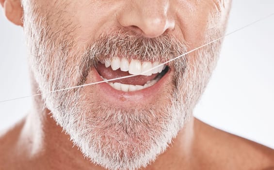 Floss, dental and face of senior man in studio isolated on a gray background. Cleaning, hygiene and elderly male model with product flossing teeth for oral wellness, tooth care and healthy mouth