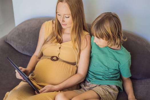 pregnant mom and son look at the tablet. Reading a book or watching a cartoon or making a video call. Look at the photo from the ultrasound.