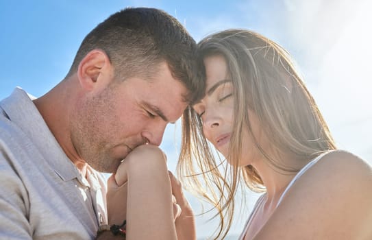 Love, hand and couple kiss at a beach, sharing intimate moment of romance at sunrise against blue sky background. Travel, freedom and man with woman embrace, care and relax in nature together mockup.