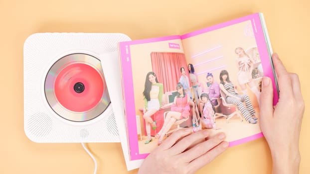 Hands holding Twice Between 1 and 2 mini Album photobook on yellow. Music CD player. South Korean girl group Twice. Space for text. Gatineau, QC Canada - December 27 2022