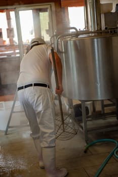 Cheesemaker cooking stirring italian bufalo organic milk in stainless steel caudrons, to produce ricotta cheese, italian food excellence worldwide export.