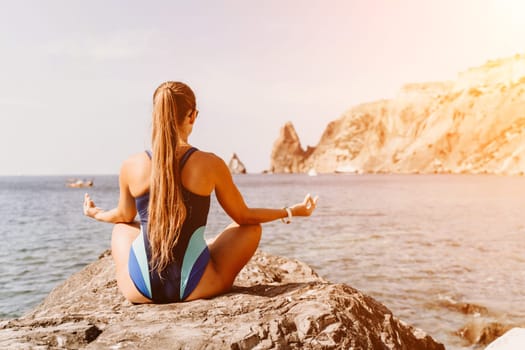 Yoga on the beach. A happy woman meditating in a yoga pose on the beach, surrounded by the ocean and rock mountains, promoting a healthy lifestyle outdoors in nature, and inspiring fitness concept