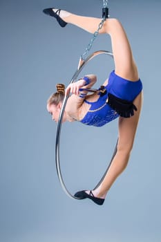 Young woman hanging in aerial ring on a blue background. The girl in a blue dancing suit
