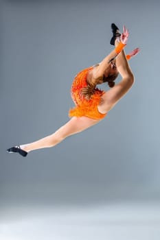 Young slim gymnast in studio. jump. Gymnast on a blue background