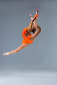 Young beautiful girl doing gymnastick jump on a blue background. The girl in the orange dancing suit