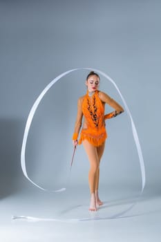teenager doing gymnastics dance with white ribbon on a blue background. The girl in the orange dancing suit