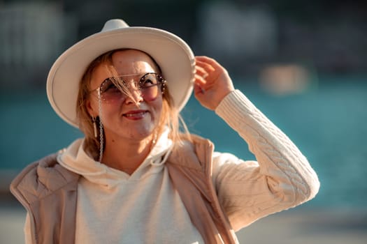 Happy blonde woman in a white suit and hat posing at the camera against the backdrop of the sea.