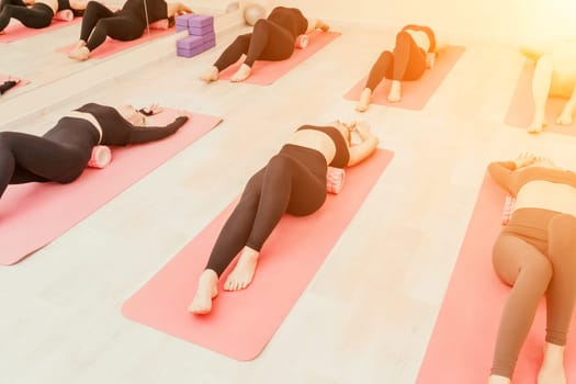 Group of young womans fitness instructor in Sportswear Leggings and Tops, stretching in the gym before pilates, on a yoga mat near the large window on a sunny day, female fitness yoga routine concept.