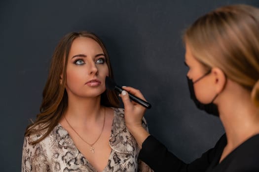 Makeup beauty salon. Makeup artist applies powder and blush. Beautiful female face. Makeup master's hand puts blush on cheeks of beauty model girl. Makeup in progress.