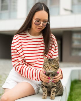 Young woman and tabby cat sitting on a bench outdoors