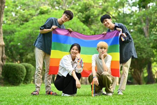 Image of young people with LGBTQ pride flag standing outdoor, supporting LGBTQ community and equality social.