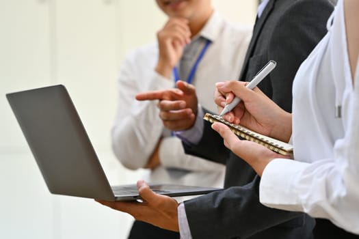 Businesspeople analyzing statistics data online on laptop screen while standing in meeting room.