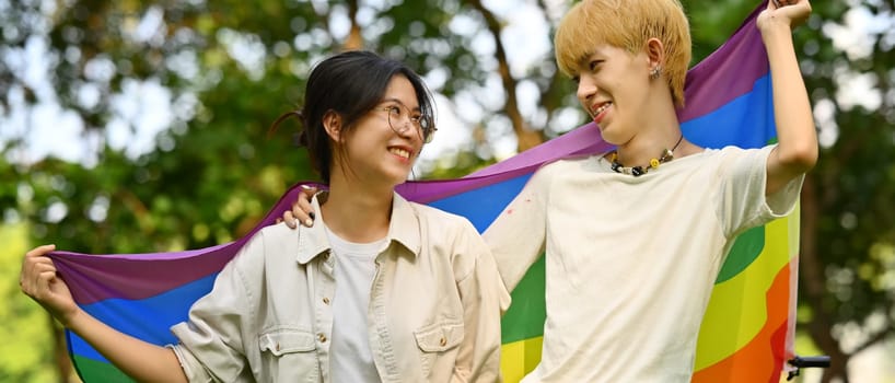 Image of young people with LGBTQ pride flag standing outdoor, supporting LGBTQ community and equality social. High quality photo