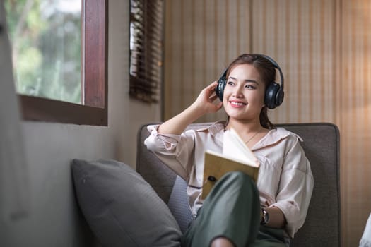 Smiling asian woman reading book at home, relaxing on a couch..