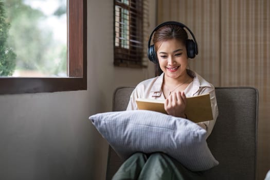 Smiling asian woman reading book at home, relaxing on a couch..