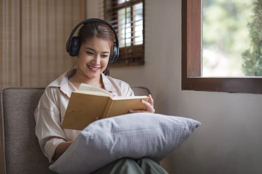 Smiling asian woman reading book at home, relaxing on a couch..