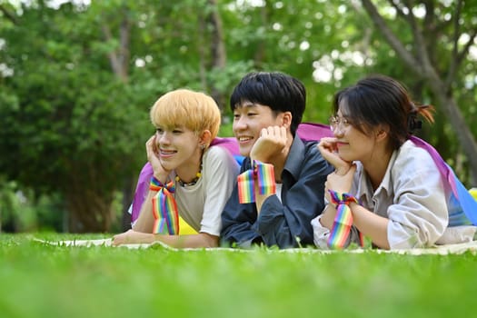 Group of LGBTQ people with pride rainbow flag, lying on green grass. LGBTQ community, freedom, solidarity and equal rights.