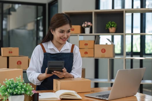 woman with Small business using calculator at workplace. Start up SME small business entrepreneurs working with boxes at home online selling ecommerce packing.
