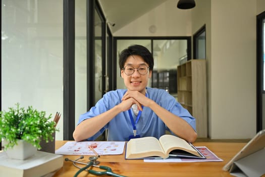 Smiling male medical students in eyeglasses reading book in library. Education and Technology concept.